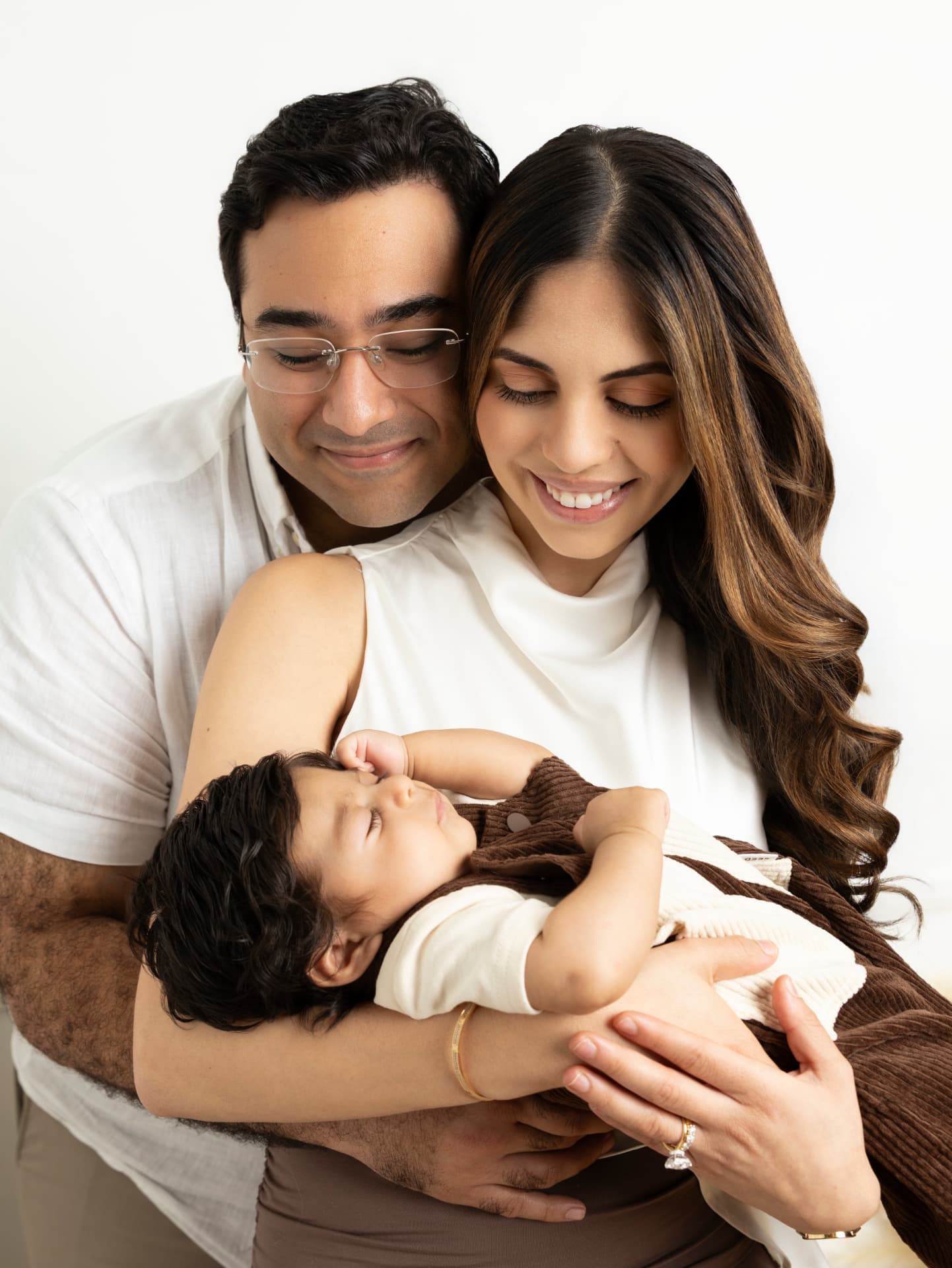 Parents smiling down at their sleeping newborn in a brown knit outfit during a studio session